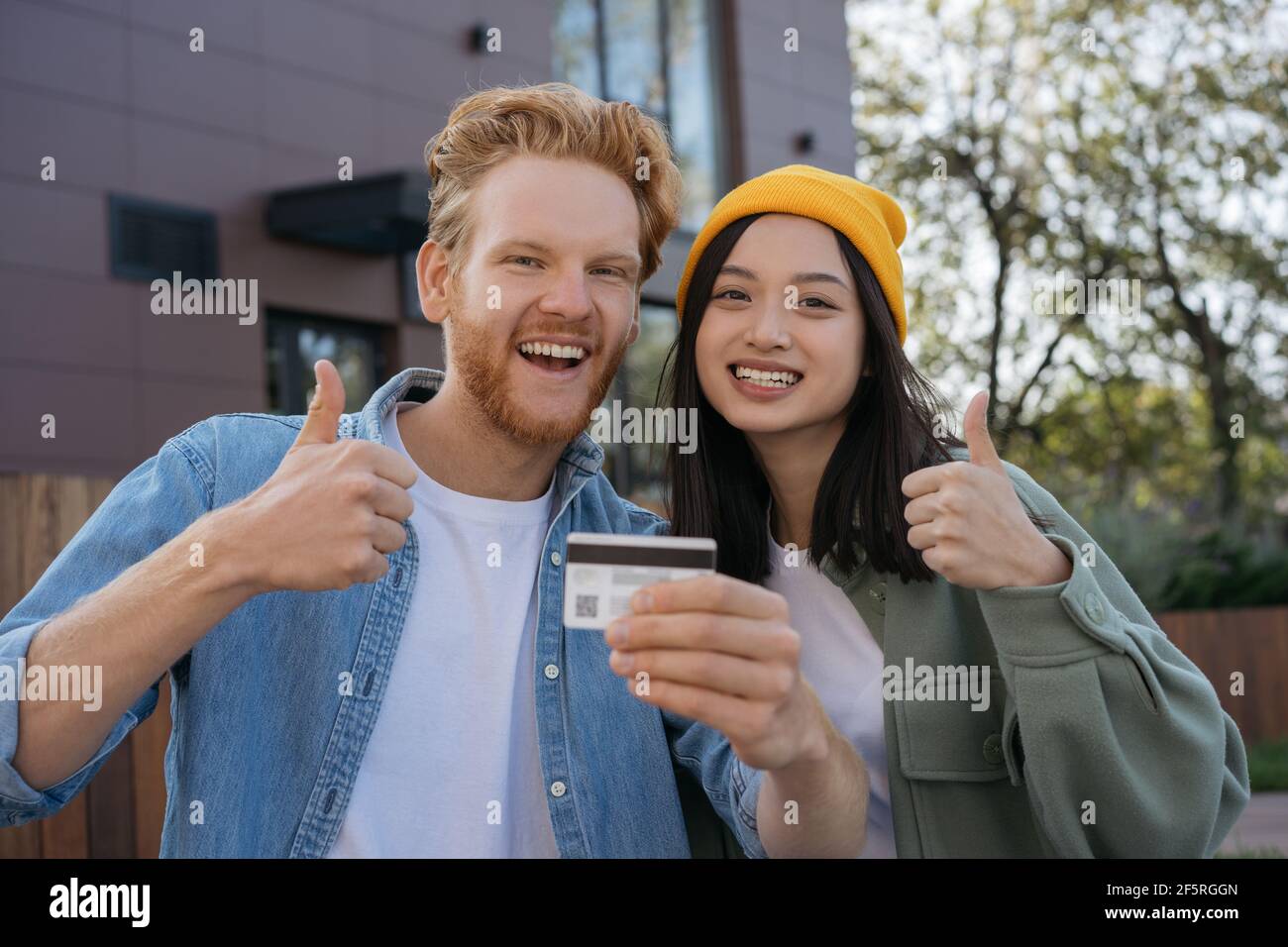Couple of smiling mixed race friends holding credit card showing thumb up looking at camera Stock Photo