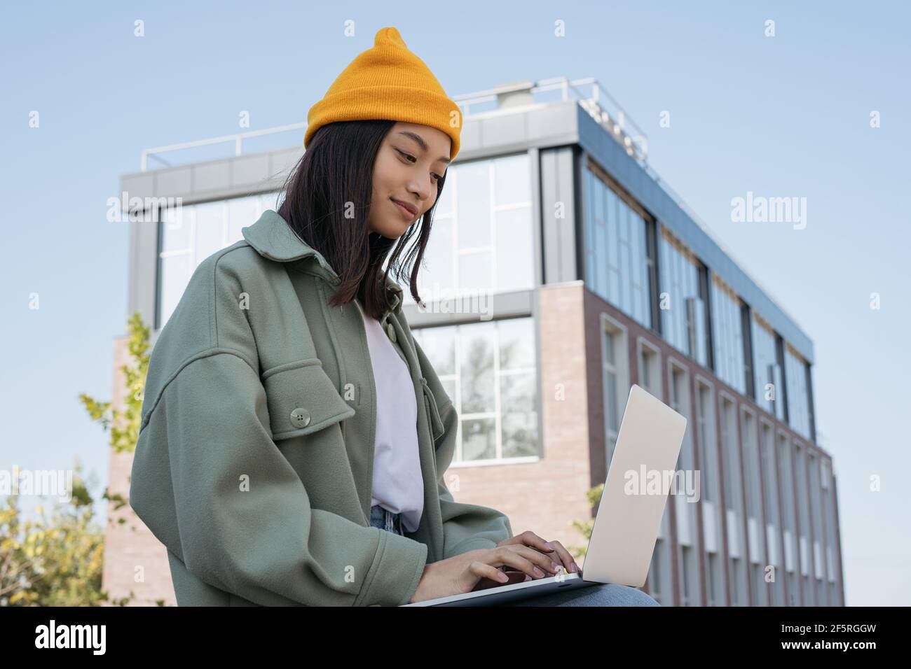 Asian woman using laptop computer, searching online. Young copywriter typing, working freelance project outdoors. University student studying Stock Photo