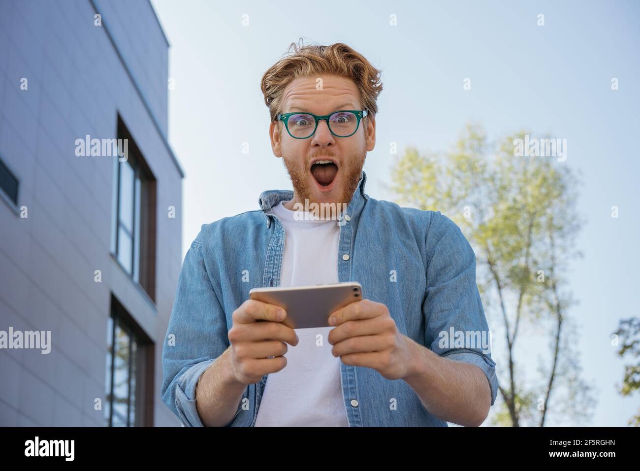 Young excited man using smartphone, playing mobile game. Portrait of overjoyed online lottery winner looking at camera. Sport betting concept Stock Photo