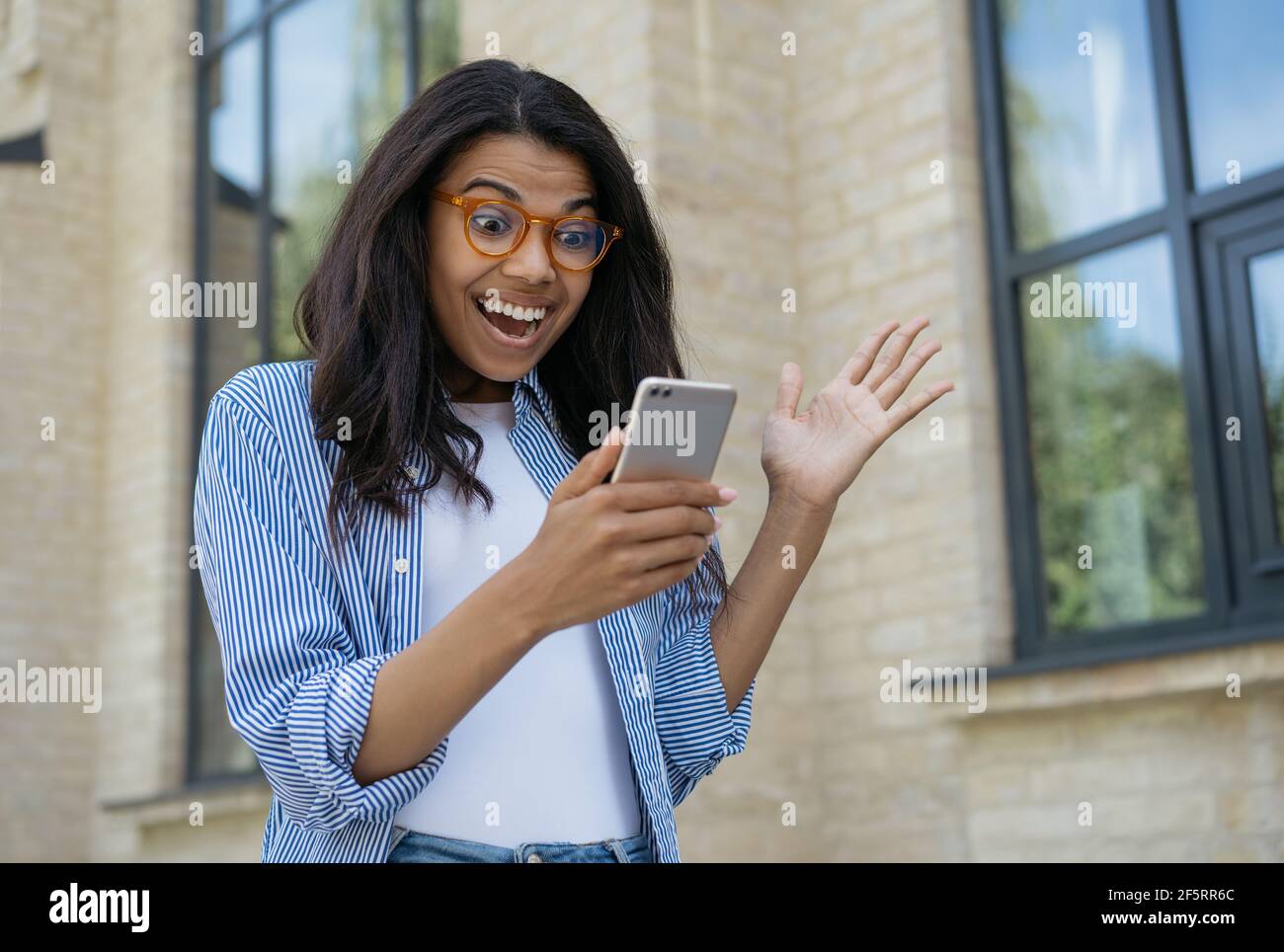 Young excited woman using smart phone shopping online. Portrait of overjoyed female playing mobile game, celebration success. Sport betting concept Stock Photo