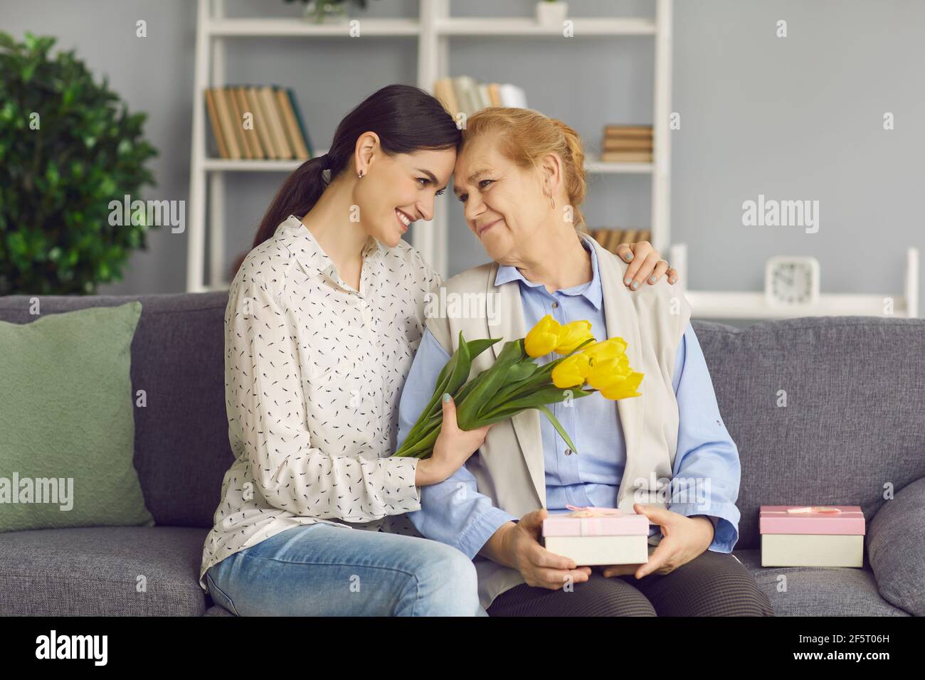 Loving daughter hugs and gives flowers and gifts to her mature mother in honor of Mother's Day. Stock Photo