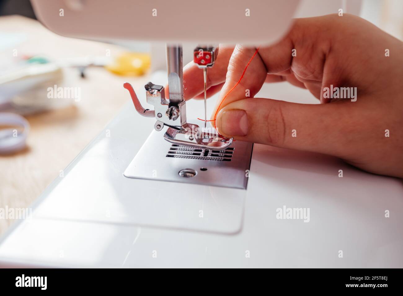 Closeup hands inserting thread into sewing machine needle Stock Photo