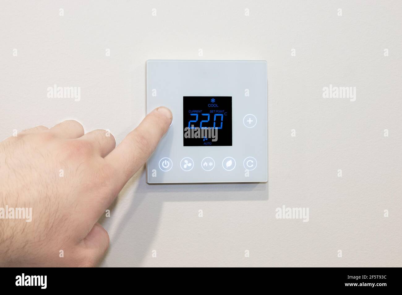 Close-up of a Caucasian male’s hand adjusting a modern wall-mounted digital thermostat Stock Photo
