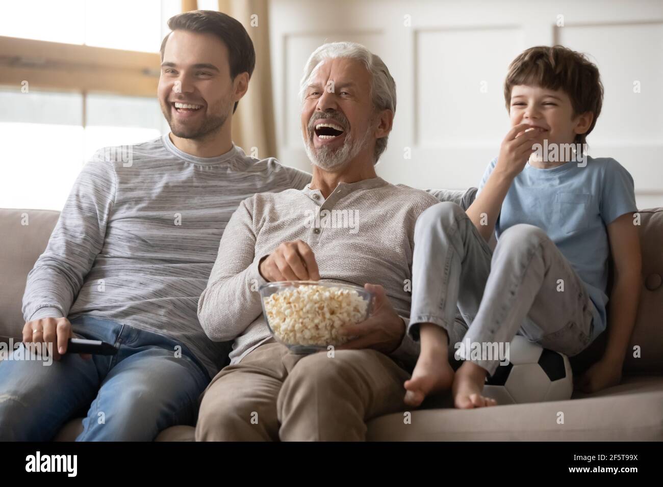 Overjoyed three generations of men watch TV Stock Photo