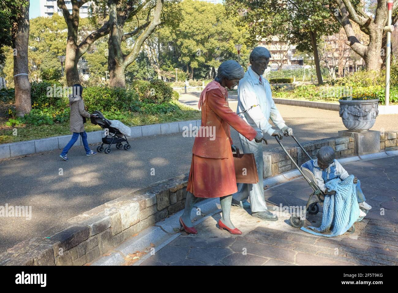 A woman pushing a pram near a model of a woman and man pushing a pram. Stock Photo