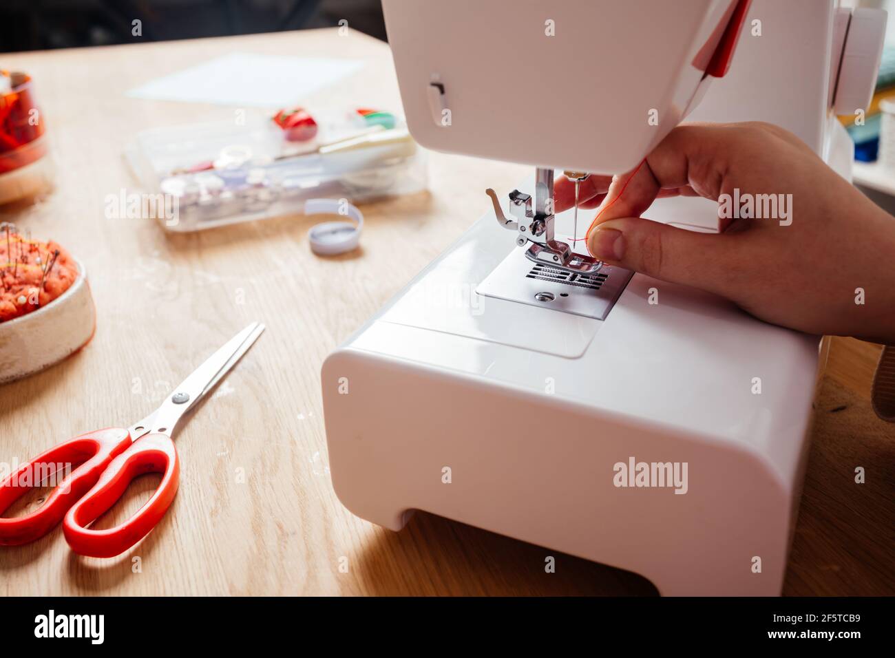 Closeup hands inserting thread into sewing machine needle Stock Photo
