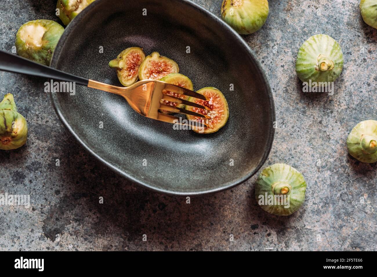 Green fig slices in modern black bowl on the table with grunge texture ...