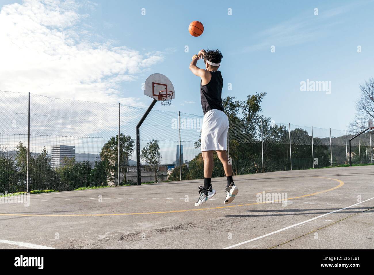 Side view of ethnic male streetball player performing slam dunk in moment of jumping above playground and scoring basketball in hoop Stock Photo