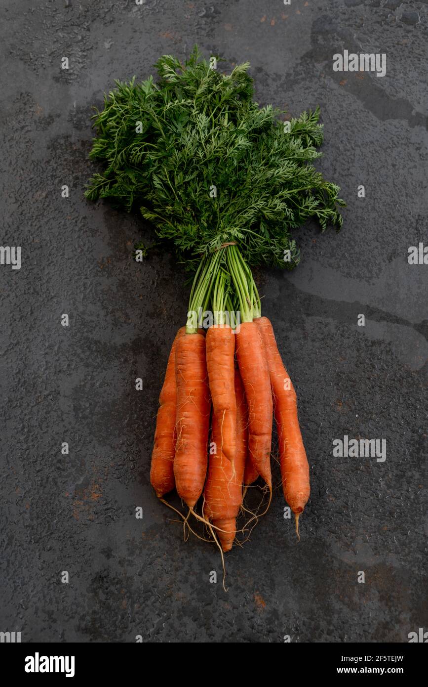 From above of bunch of ripe carrots placed on black shabby background in studio Stock Photo