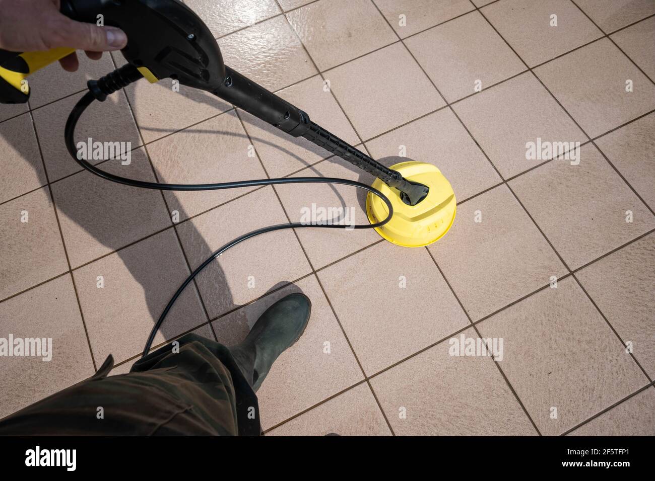 Asti-italy-March 2021 Man cleans a terrace with a special pressure brush connected to a pressure washer. Stock Photo