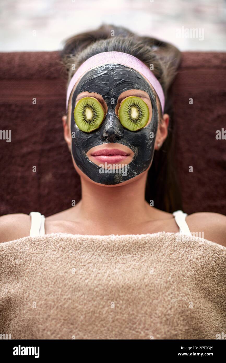 Woman with nutritious black mask on face and slice of kiwi on eyes Stock  Photo - Alamy