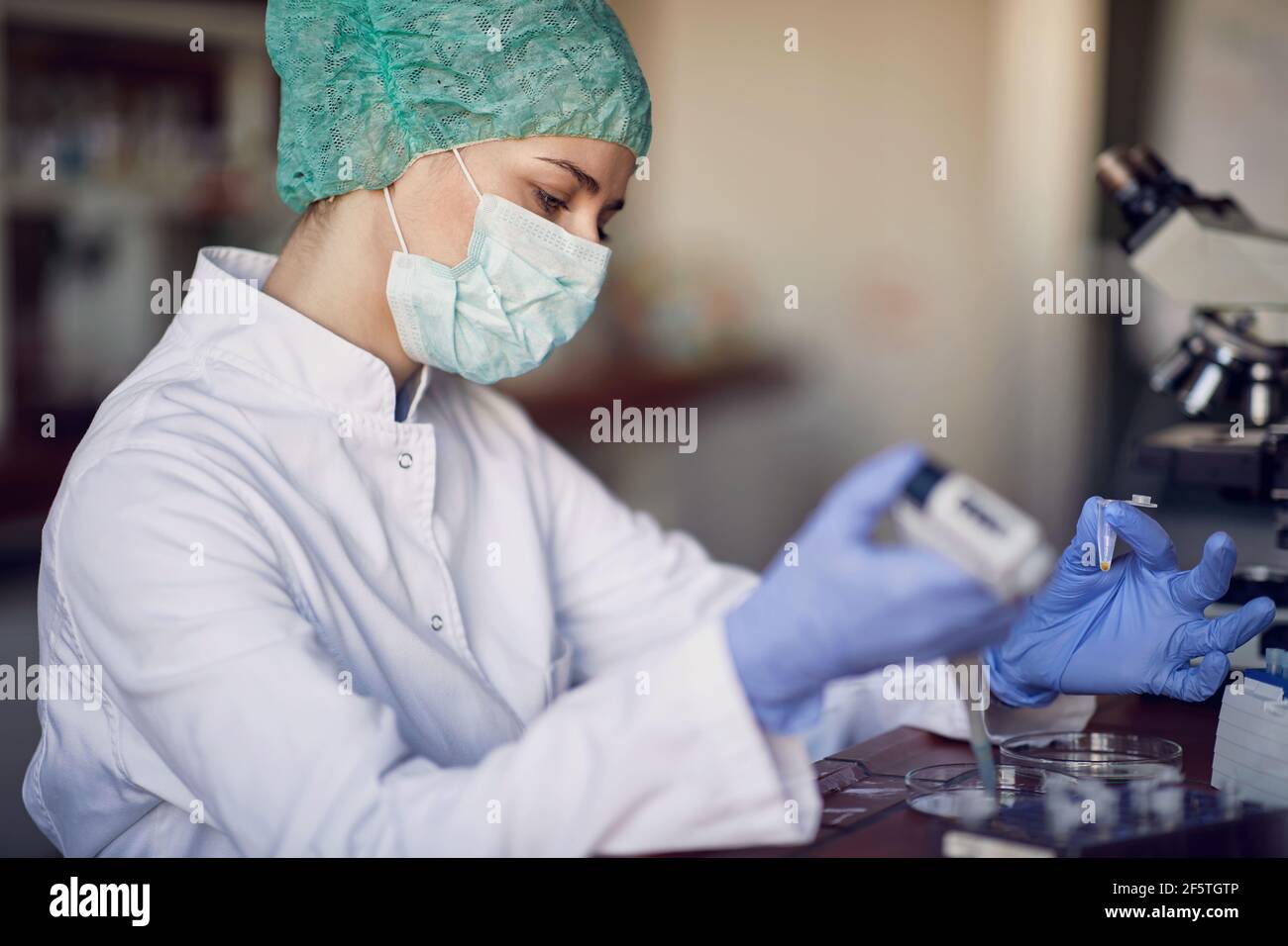A young female scientist in a protective gear preparing samples for analyses in a working atmosphere at the laboratory. covid 19, virus, corona, Scien Stock Photo