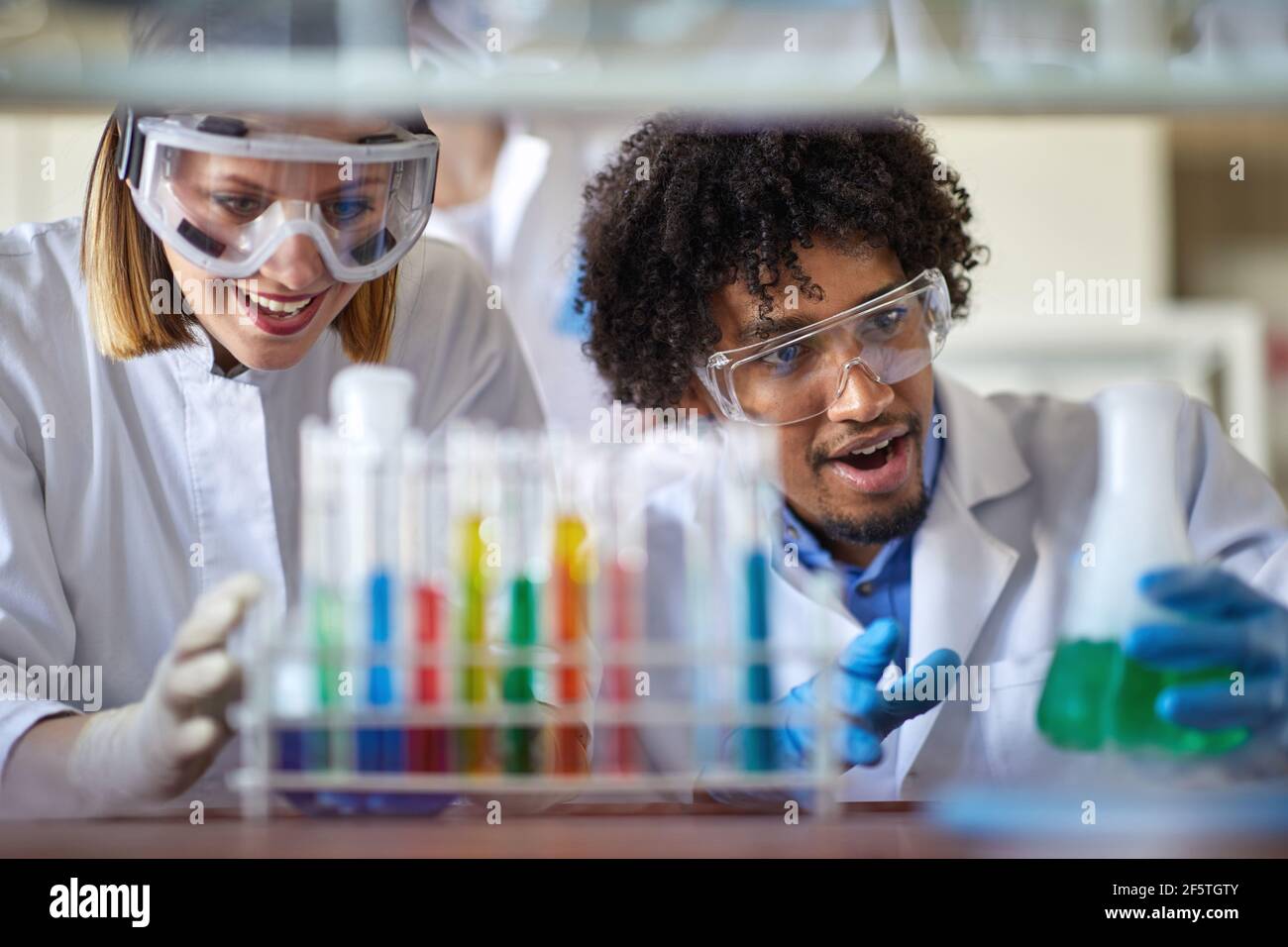 Young colleagues in a protective gear observe chemical reactions in a working atmosphere at the university laboratory. Science, chemistry, lab, people Stock Photo