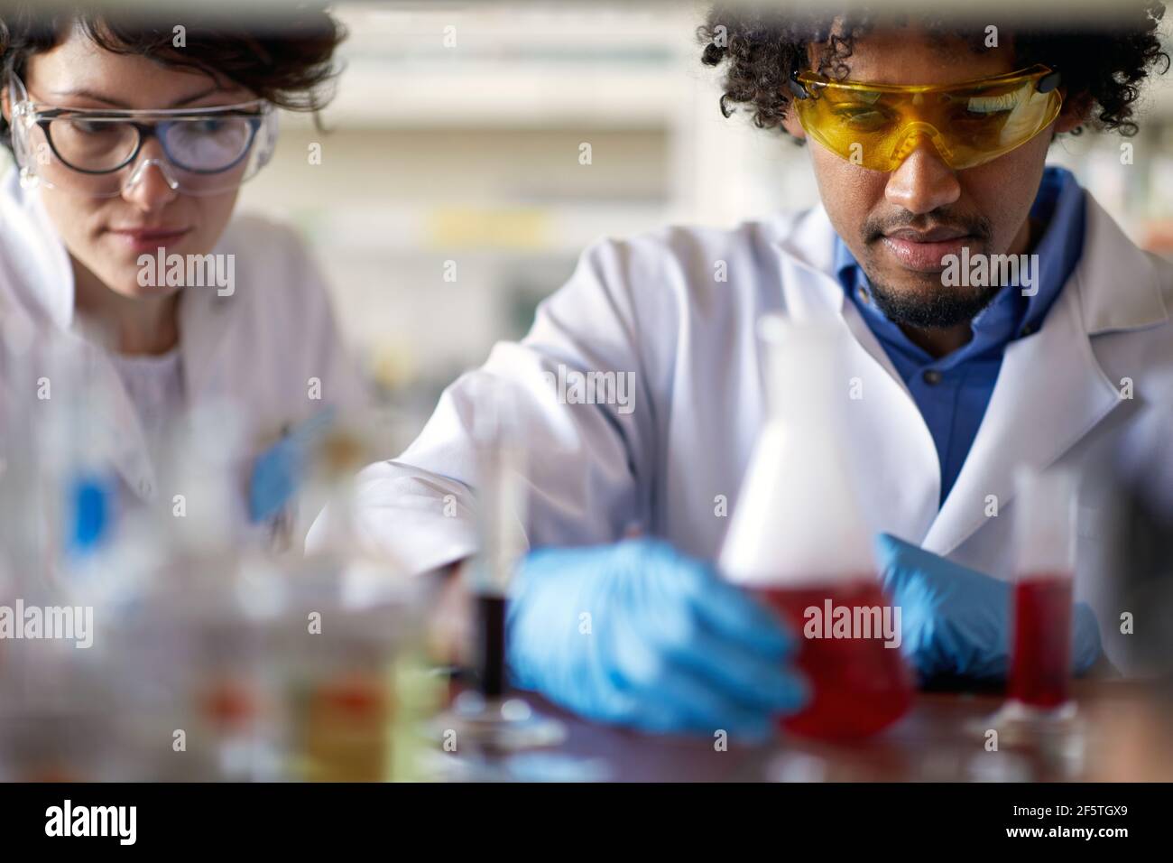 Young scientists in a protective gear observe chemical reactions in the sterile laboratory environment. Science, chemistry, lab, people Stock Photo