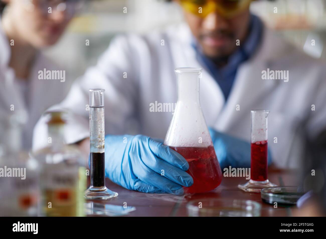 Young scientists in a protective gear observe chemicals in test tubes in the sterile laboratory environment. Science, chemistry, lab, people Stock Photo