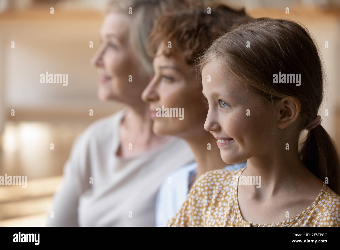 Smiling three generations of women look in distance Stock Photo
