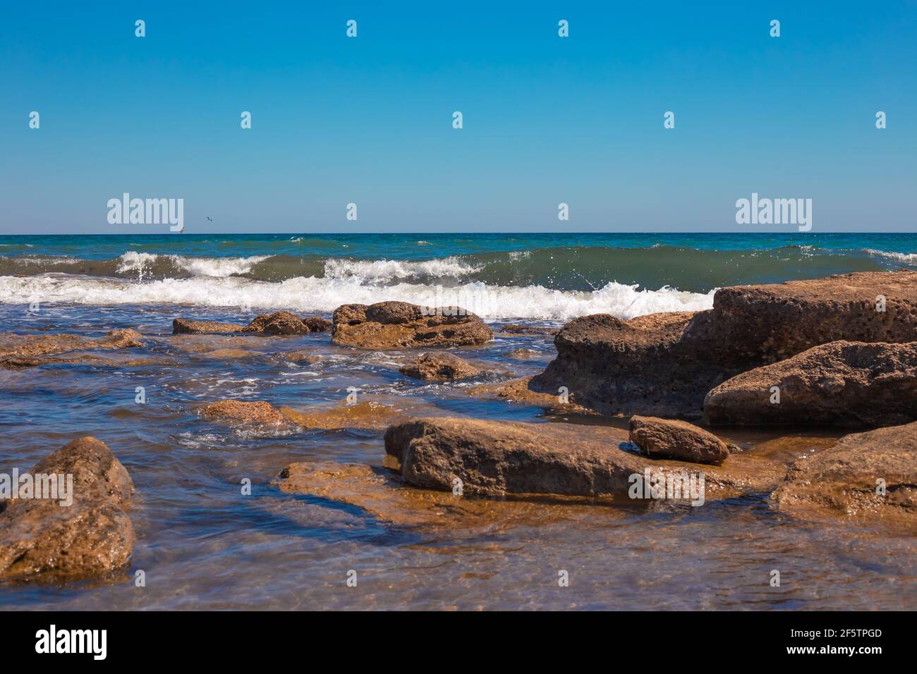 Seashore with a blue wave beating against the stones on the beach. Sea sunny summer landscape. Stock Photo
