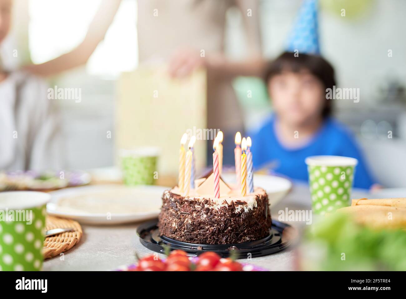 Close up of a birtday cake with candles on the table. Happy hispanic family with kids celebrating birthday at home Stock Photo