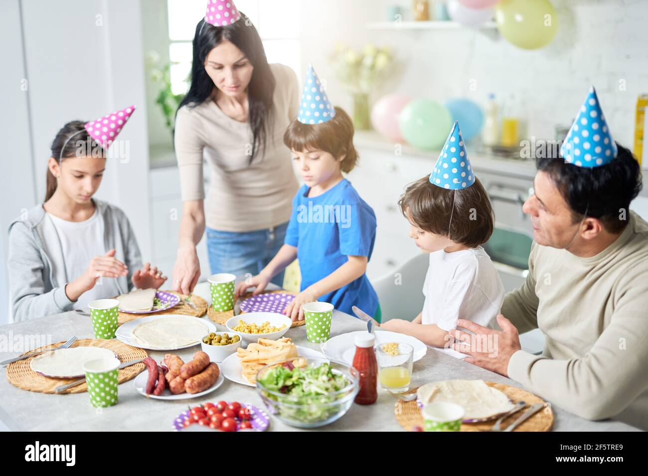 Preparation. Caring latin middle aged mother serving her family while they having dinner, celebrating birthday together at home Stock Photo