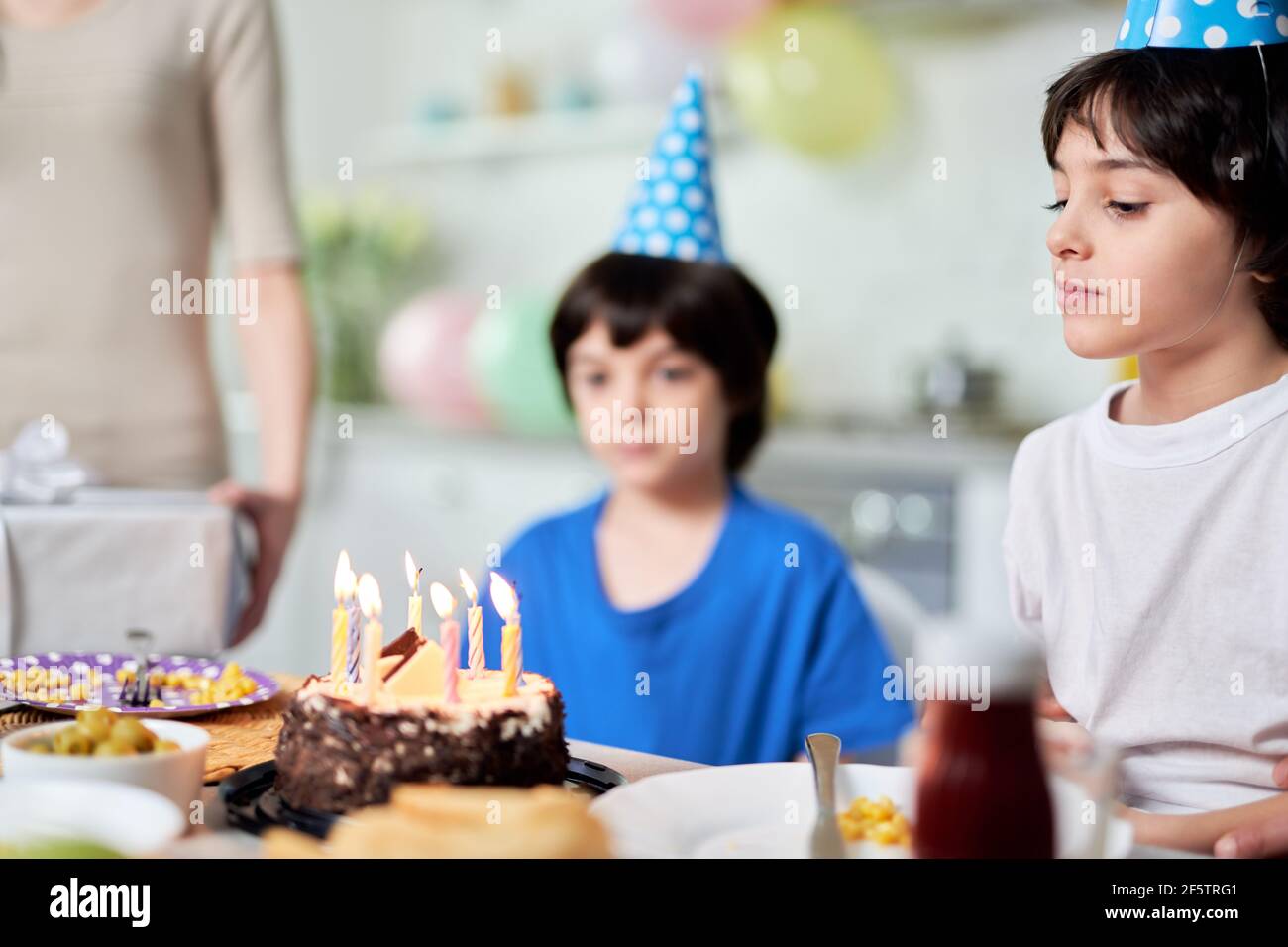Happy moment. Close up of little hispanic boy looking at birthday cake, making a wish while getting ready for blowing candles. Latin family Stock Photo