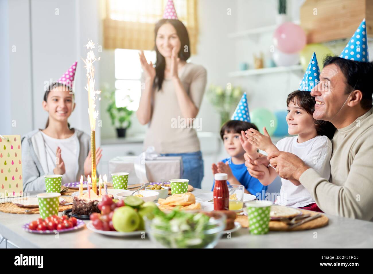 Family party. Happy latin american family with children looking suprised about firework sparkler on a cake while celebrating birthday together at home Stock Photo