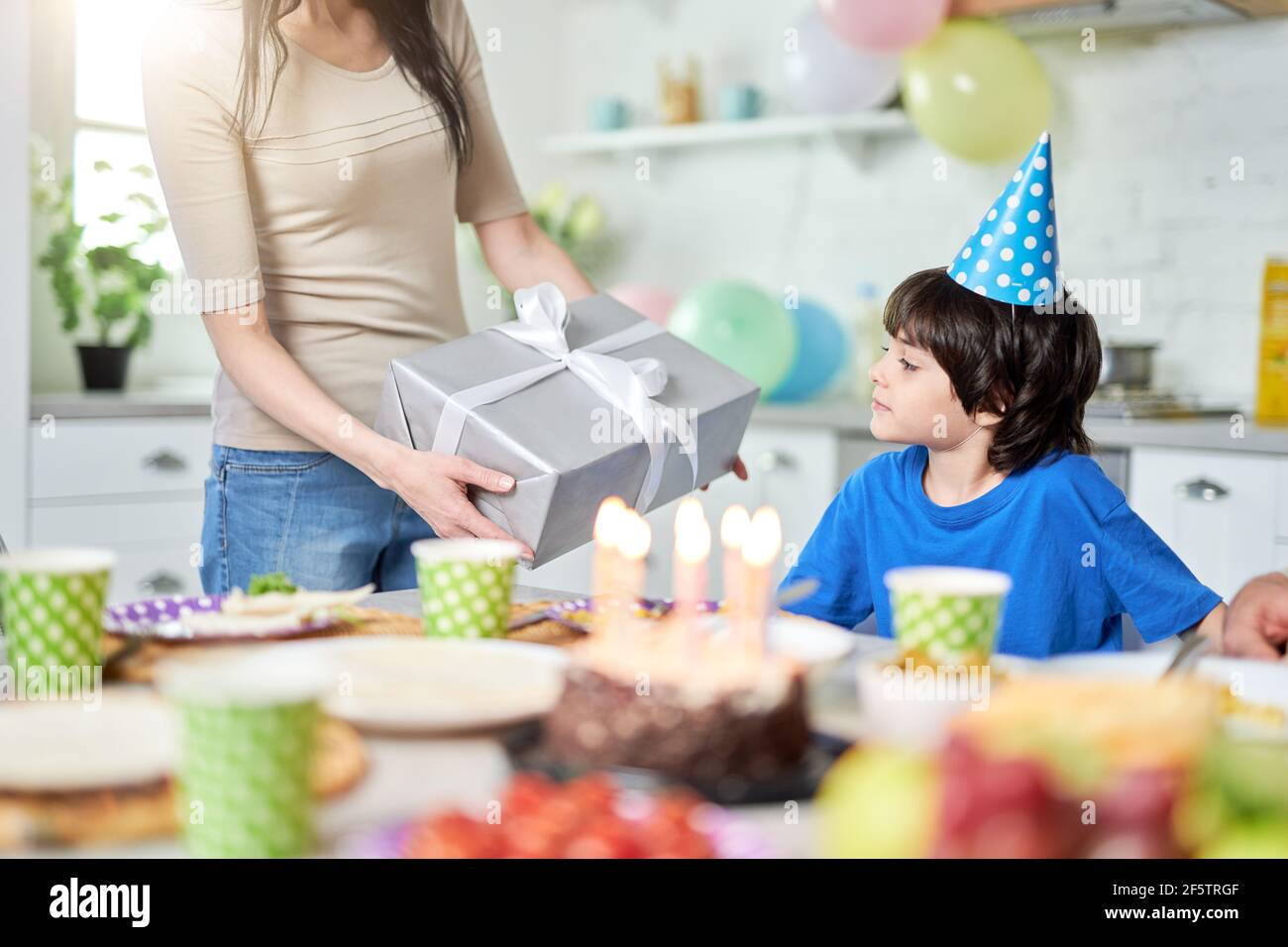 Surprise. Mother gives gift box to her lovely little boy, while having dinner, celebrating child s birthday at home Stock Photo