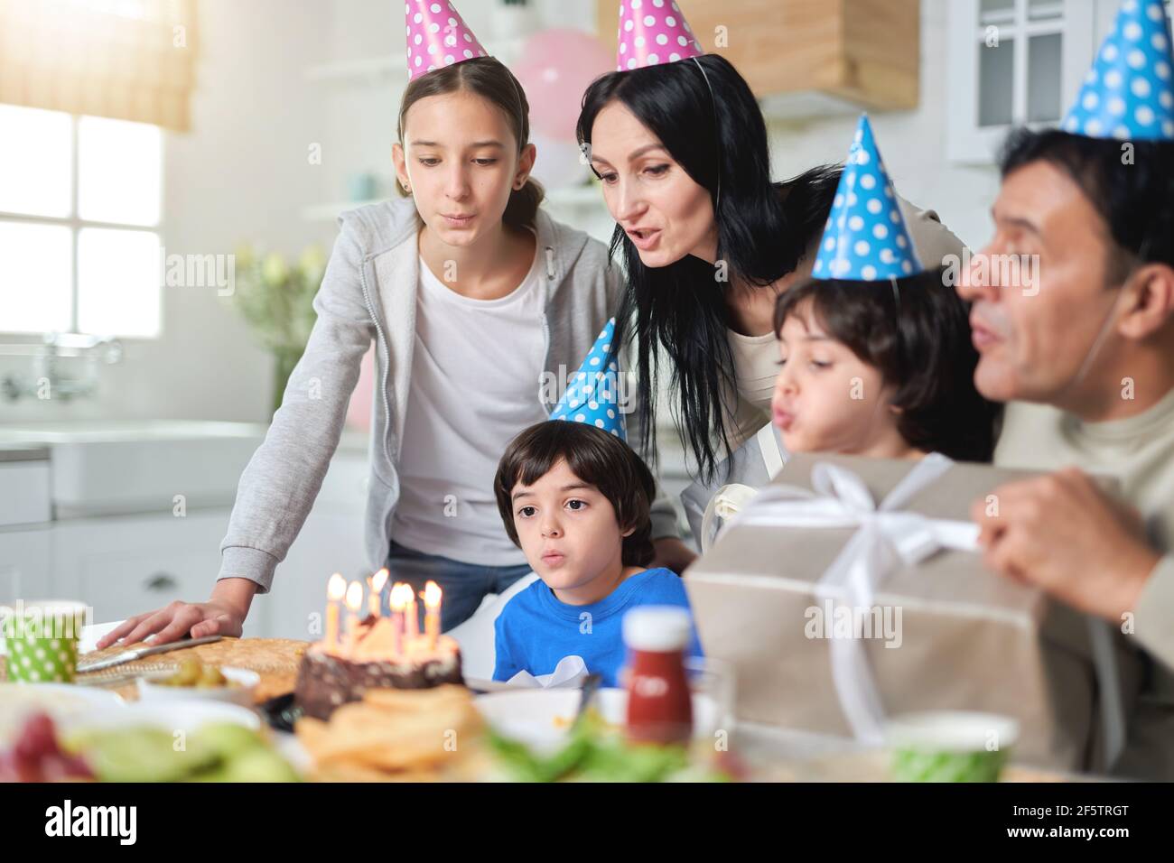 Cheerful latin american family wearing birthday caps, blowing candles on a cake while celebrating birthday together at home Stock Photo