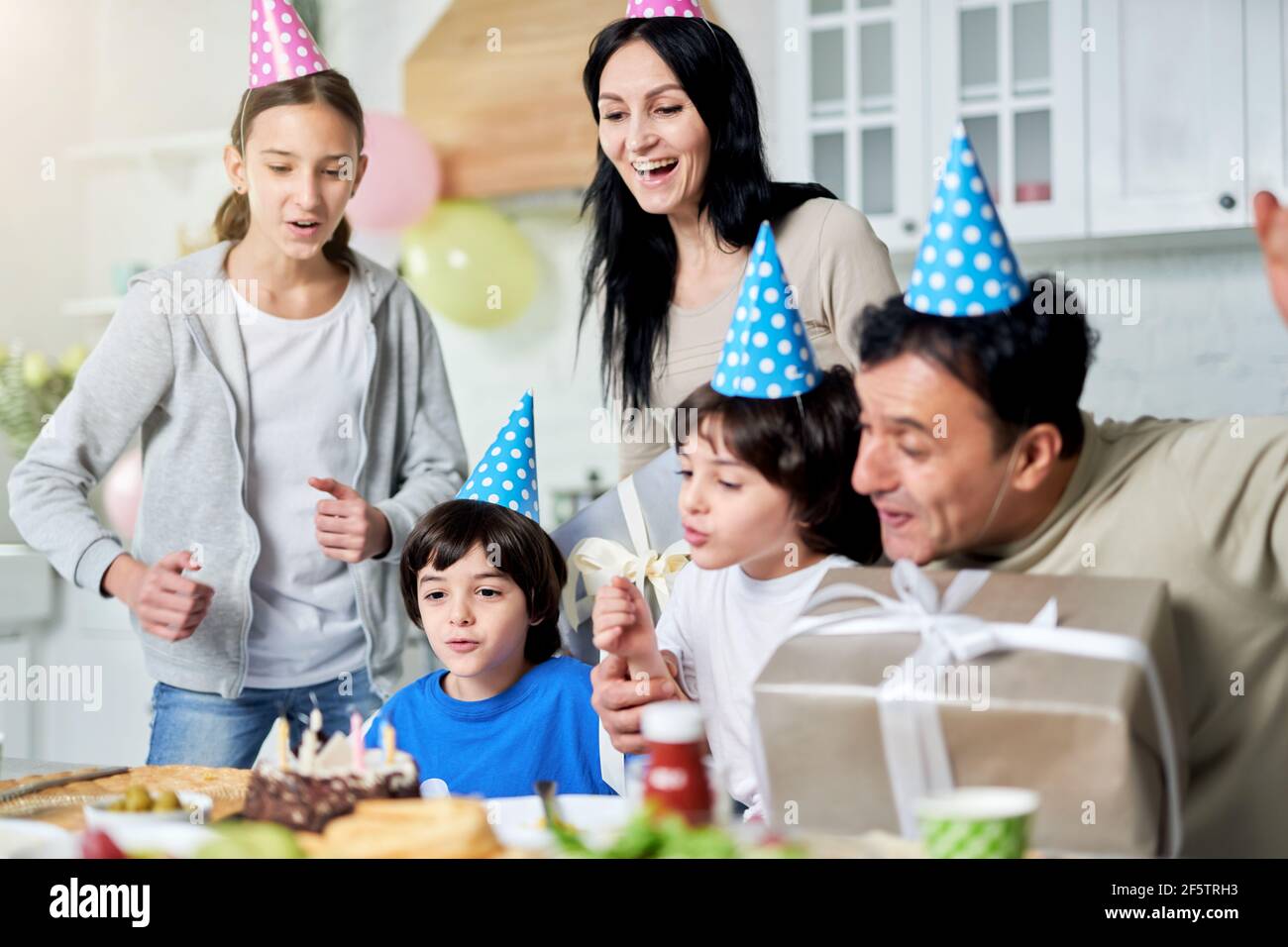 Pure joy. Joyful latin family with children wearing birthday caps, celebrating birthday together at home Stock Photo
