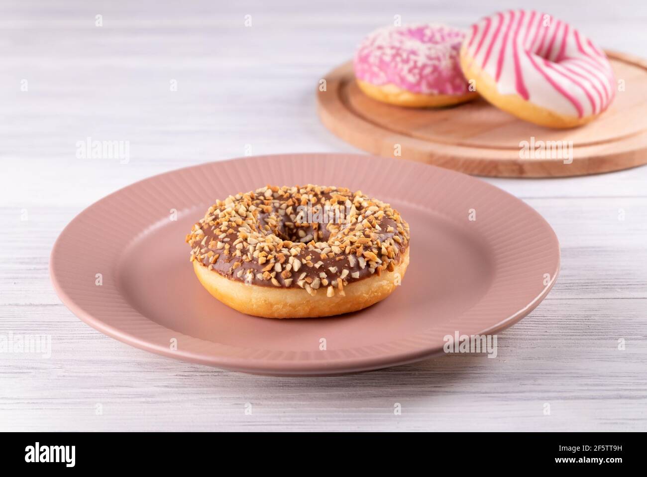 Three sugar-coated donuts lie on a pink ceramic plate and a wooden cutting board. Stock Photo