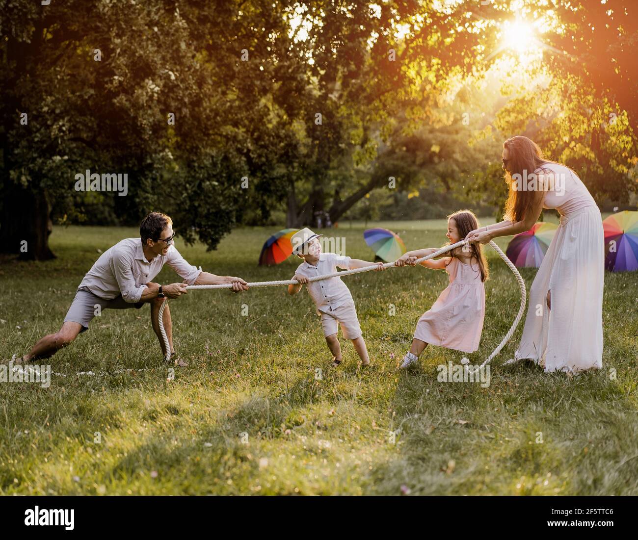 Joyful, young family playing tug-of-war in the park Stock Photo