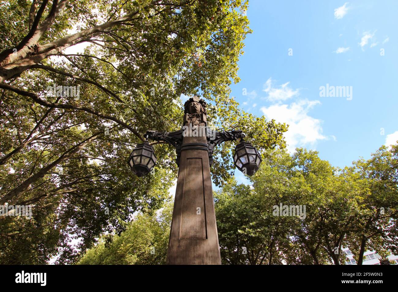 Wide-angle view of an old stone lantern on the historic 'Königsallee' in downtown Düsseldorf, surrounded by green trees. Stock Photo