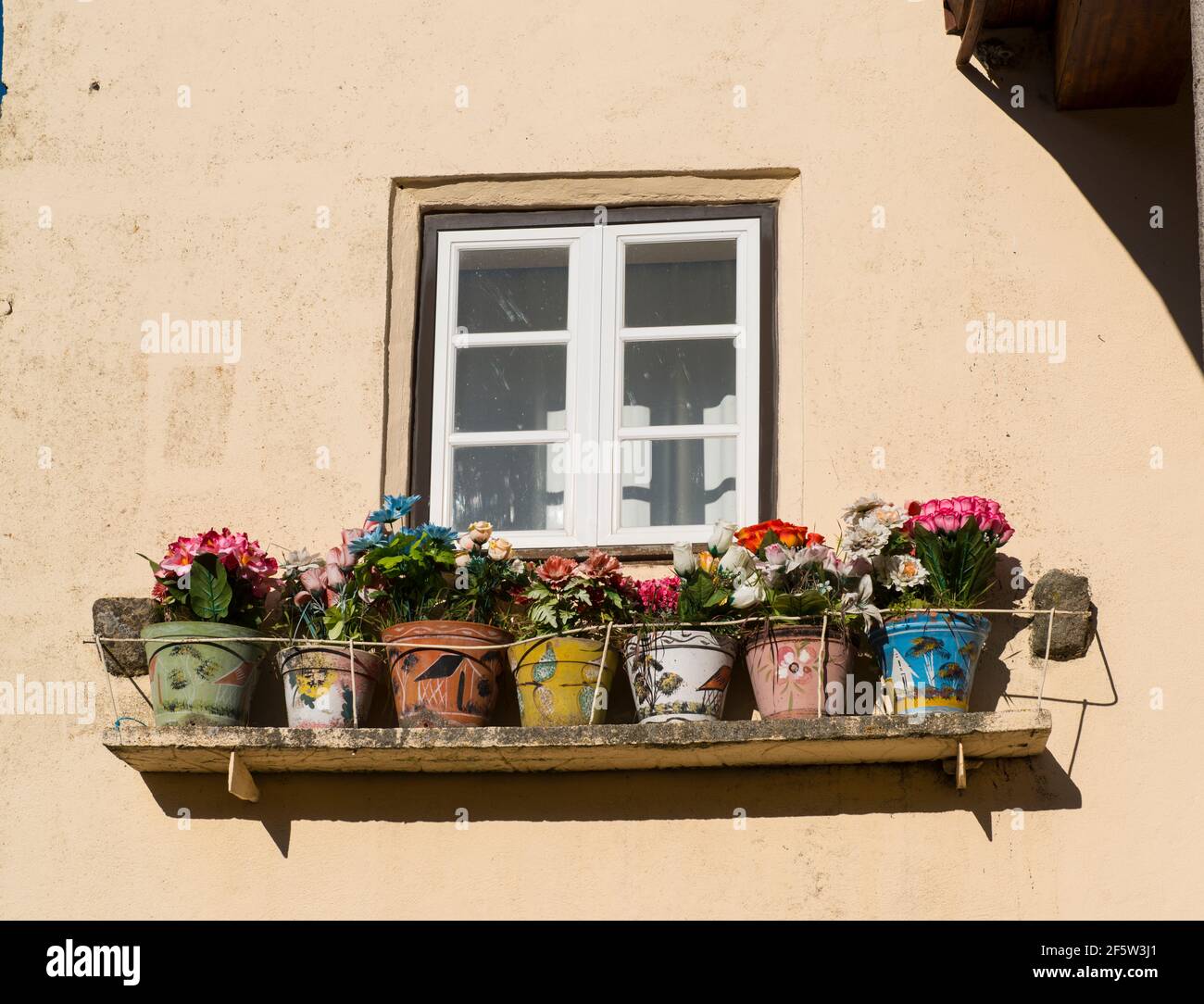 The village Castelo Mendo, Almeida district, Portugal. Flowerpots with colorful artificial flowers under a window Stock Photo