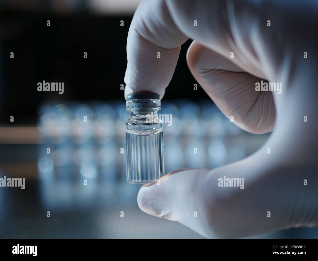 Filled vial hold by fingers in a glove Stock Photo Alamy