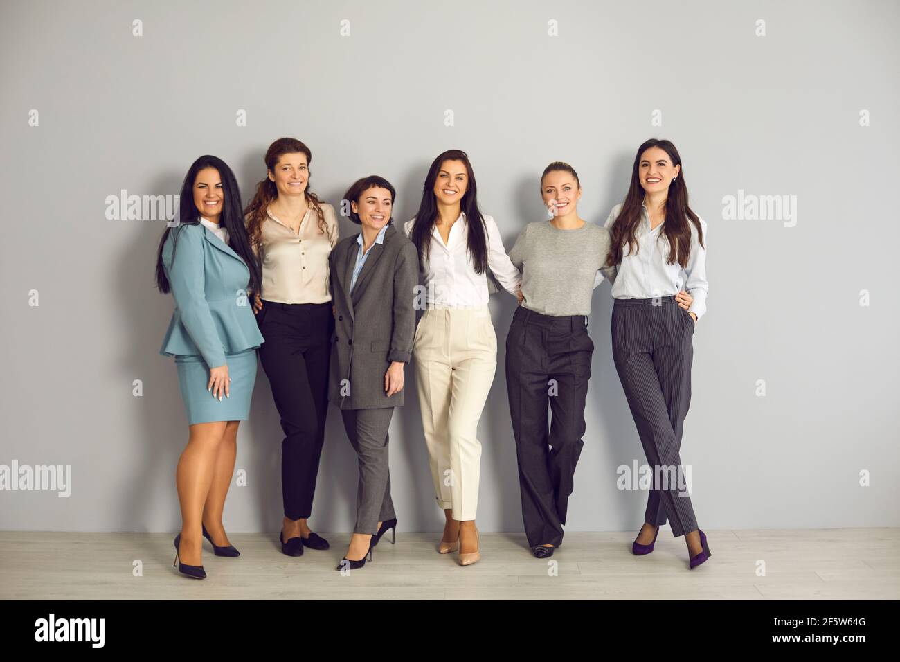 Group portrait of successful and stylish business women posing against gray wall background. Stock Photo