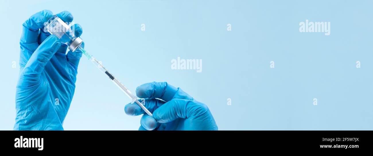 gloved doctor hands fill vial syringe on blue background in banner format with copy space Stock Photo