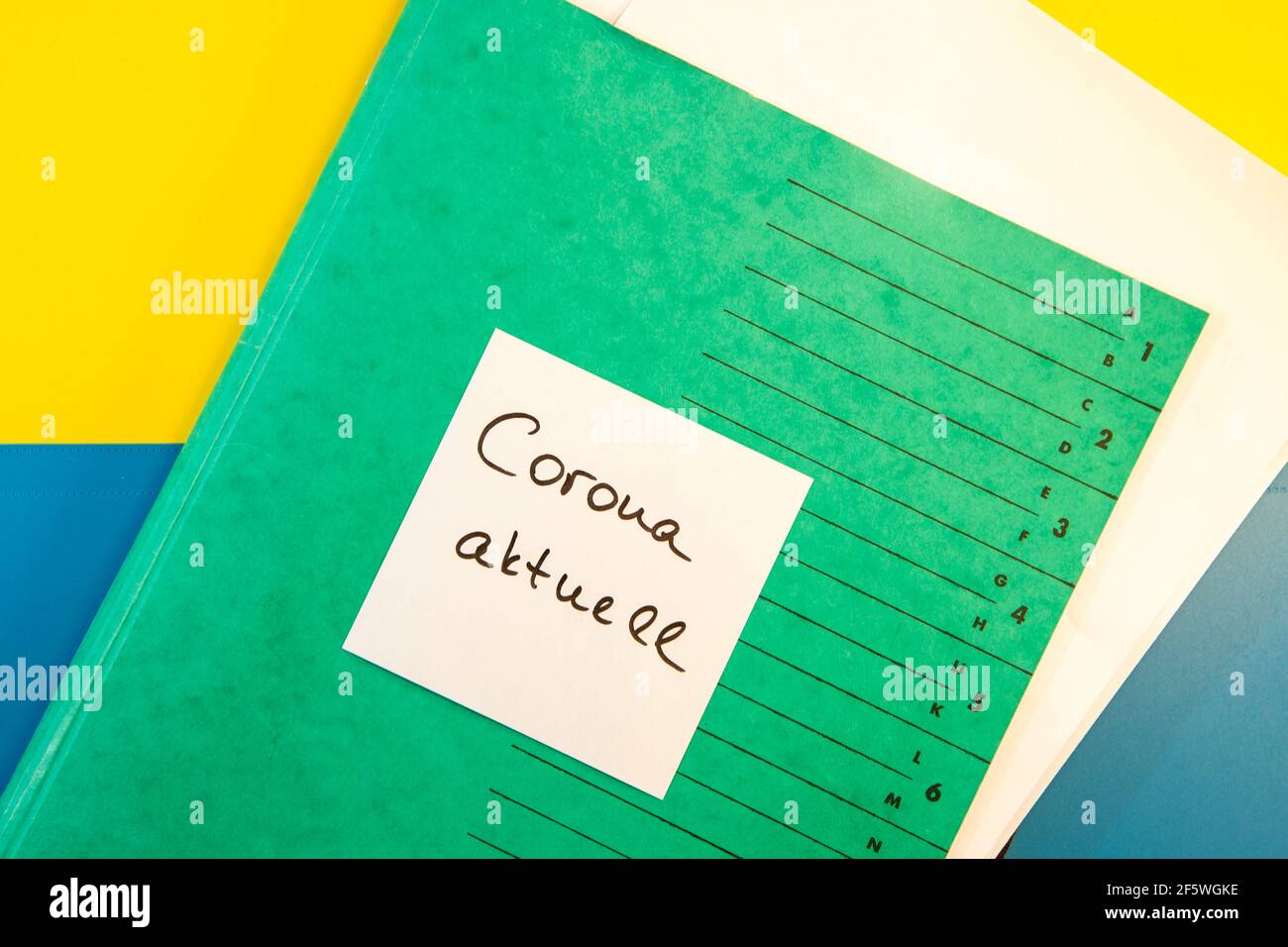 Green Folder with empty sticky note message, text paper note with Corona aktuell means News and Documents. abstract yellow blue paper Background. copy Stock Photo