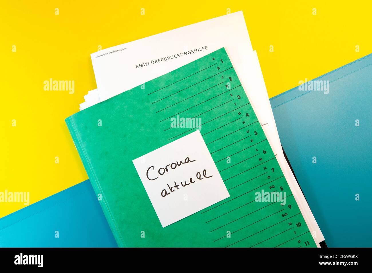 Green folder with a lot of paper. BMWI Überbrückungshilfe, paper note Corona aktuell. German application form allowance, Corona Soforthilfe Stock Photo