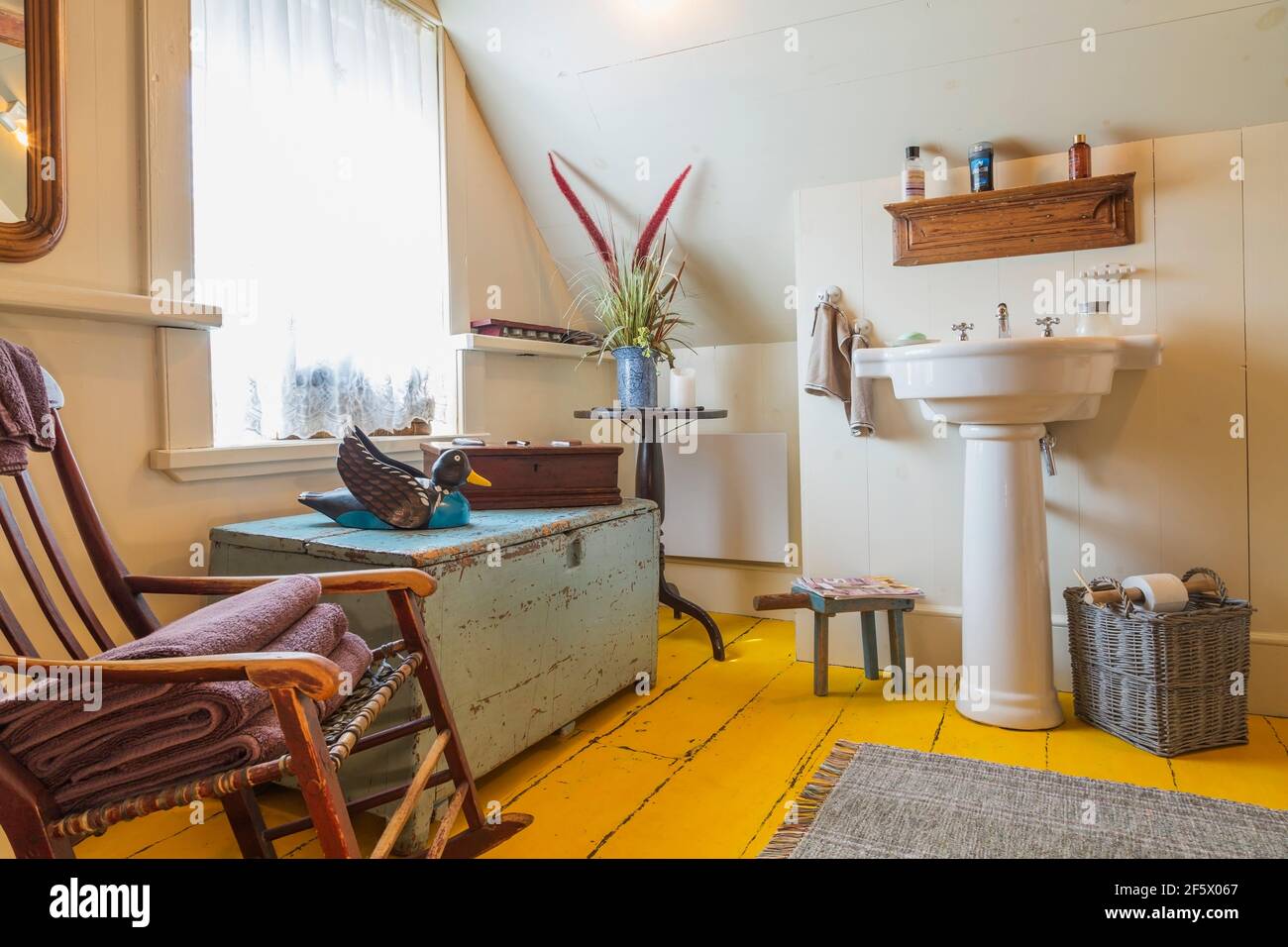 White pedestal sink, wicker basket, antique blue pine wood chest, rocking chair in bathroom on upstairs floor inside an old circa 1790 Canadiana home Stock Photo
