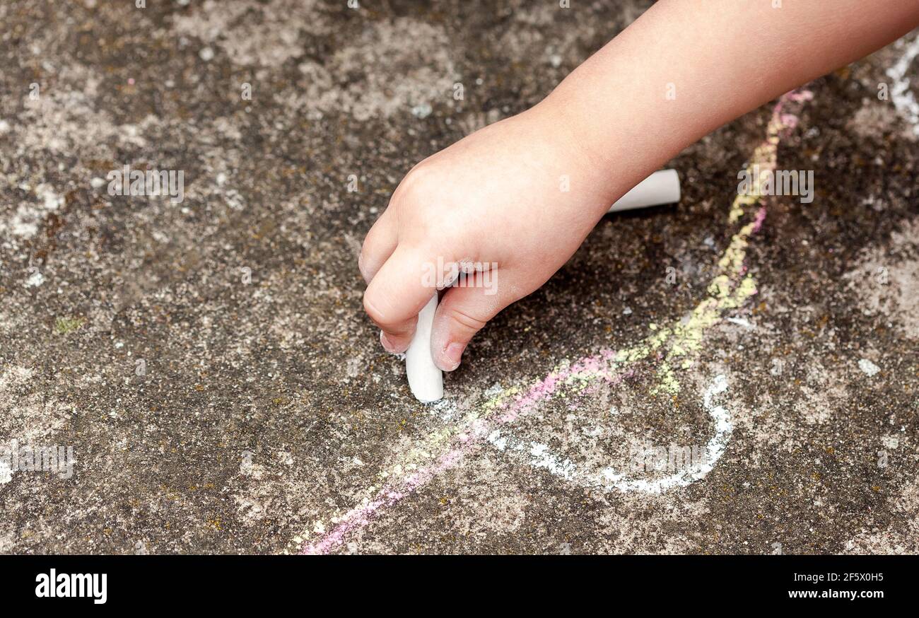 Little child's hand, girl holding white chalk, drawing, writing on the