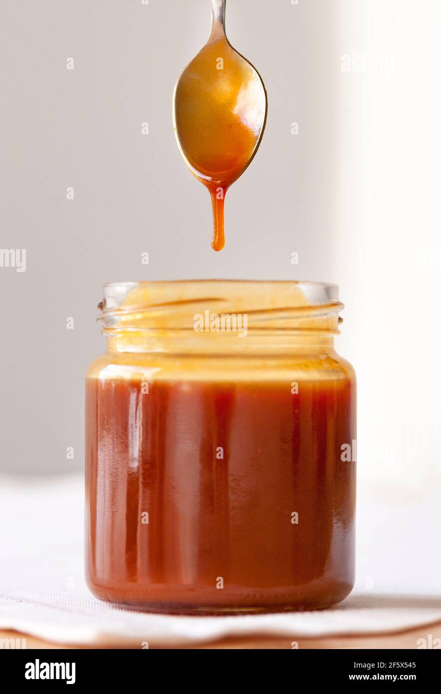 Jar of delicious homemade caramel with a drop falling from a spoon Stock Photo