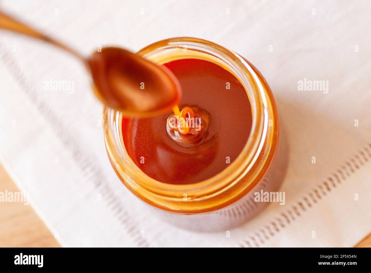 Jar of delicious homemade caramel with a drop falling from a spoon Stock Photo
