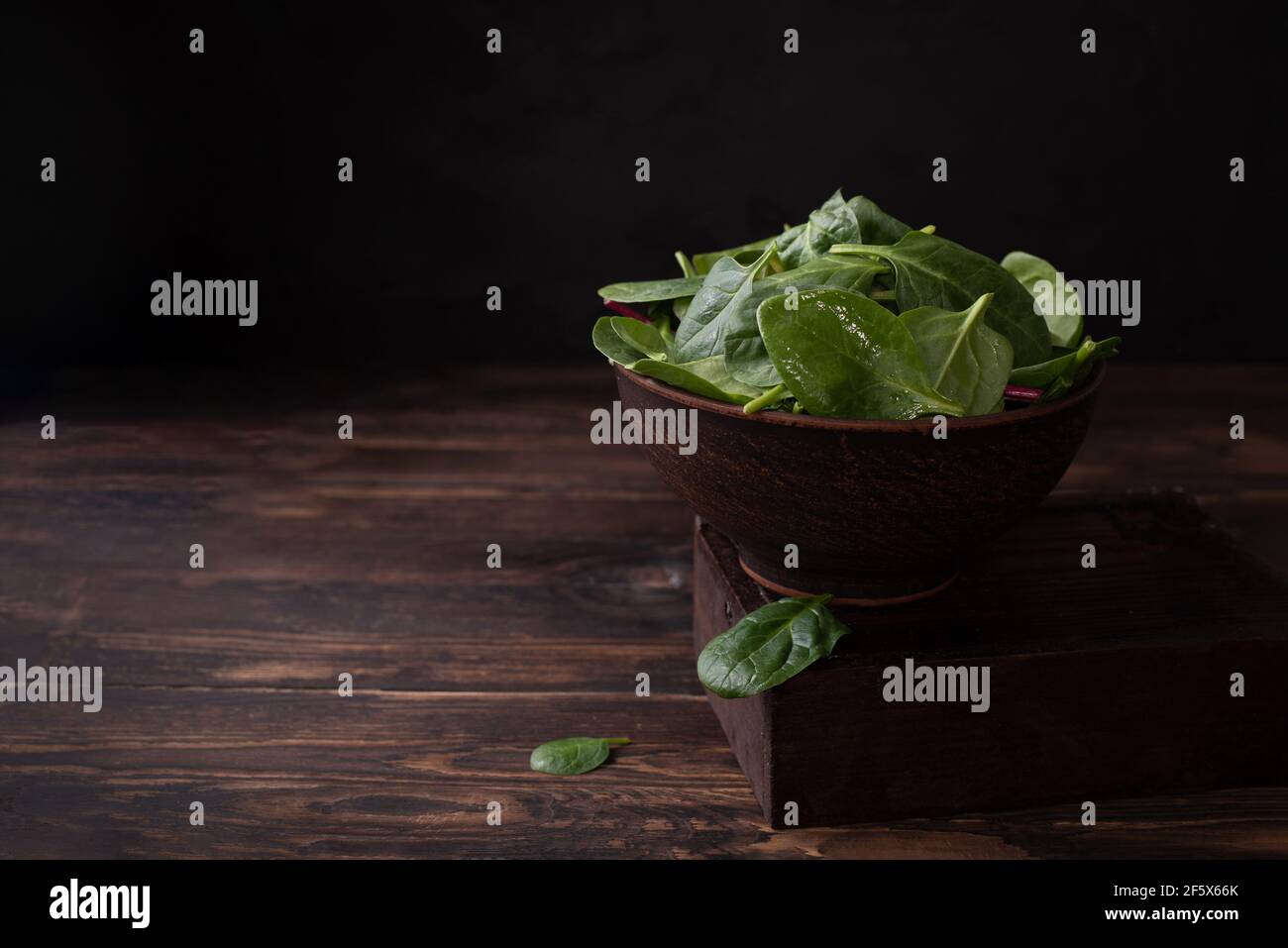 Bowl with baby spinach on a dark wooden background, healthy eating, rustic style, close up. Stock Photo