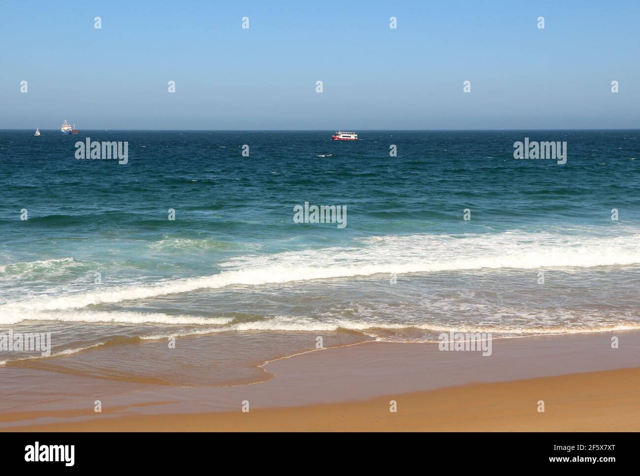 Beach view with a Regina ferry tourist boat on rough seas and an anchored ship on a windy spring afternoon Santander Cantabria Spain Stock Photo