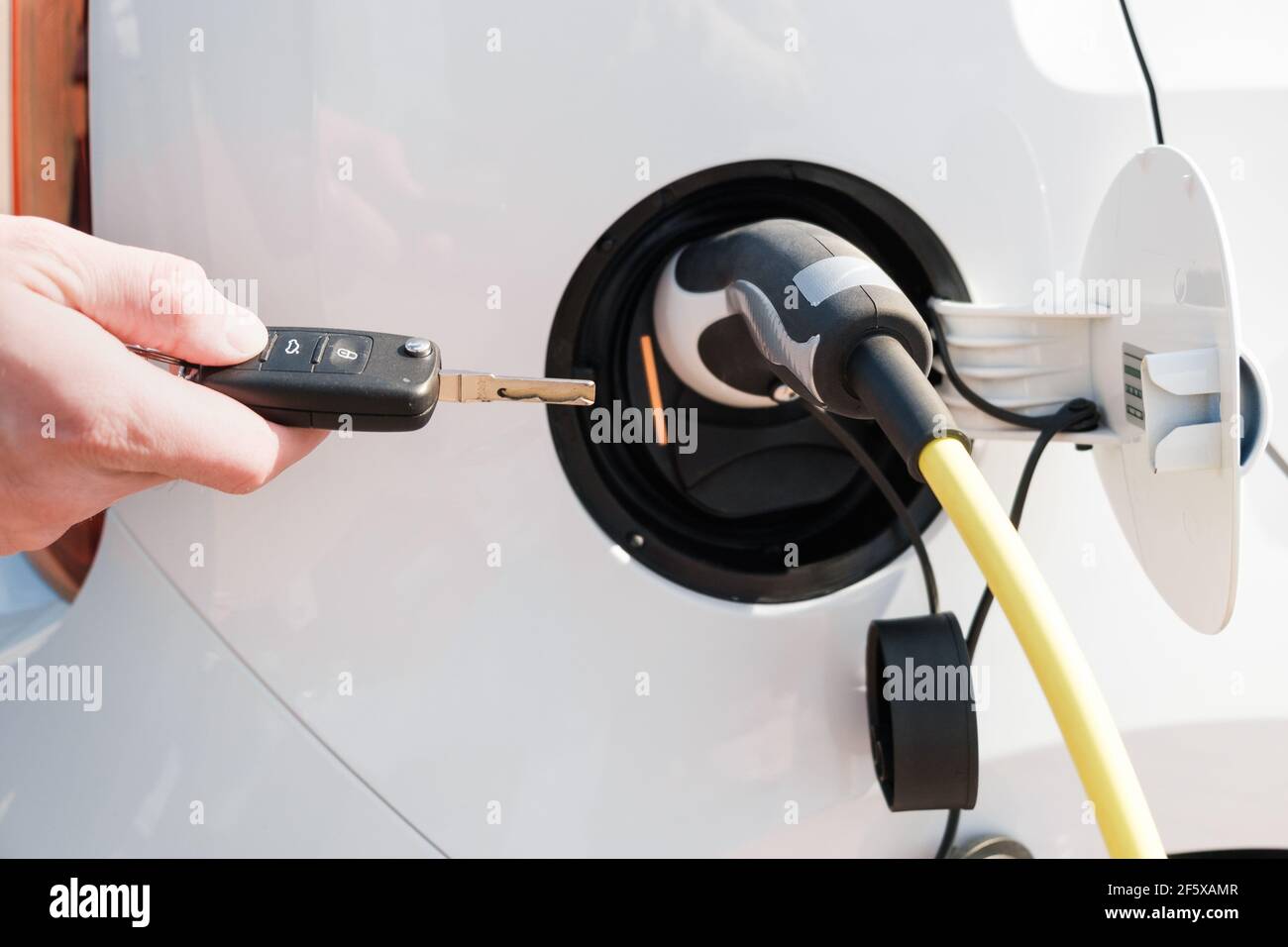 Charging an electric vehicle with a power cable supply plugged in and mans hand unblocking it with a key Stock Photo