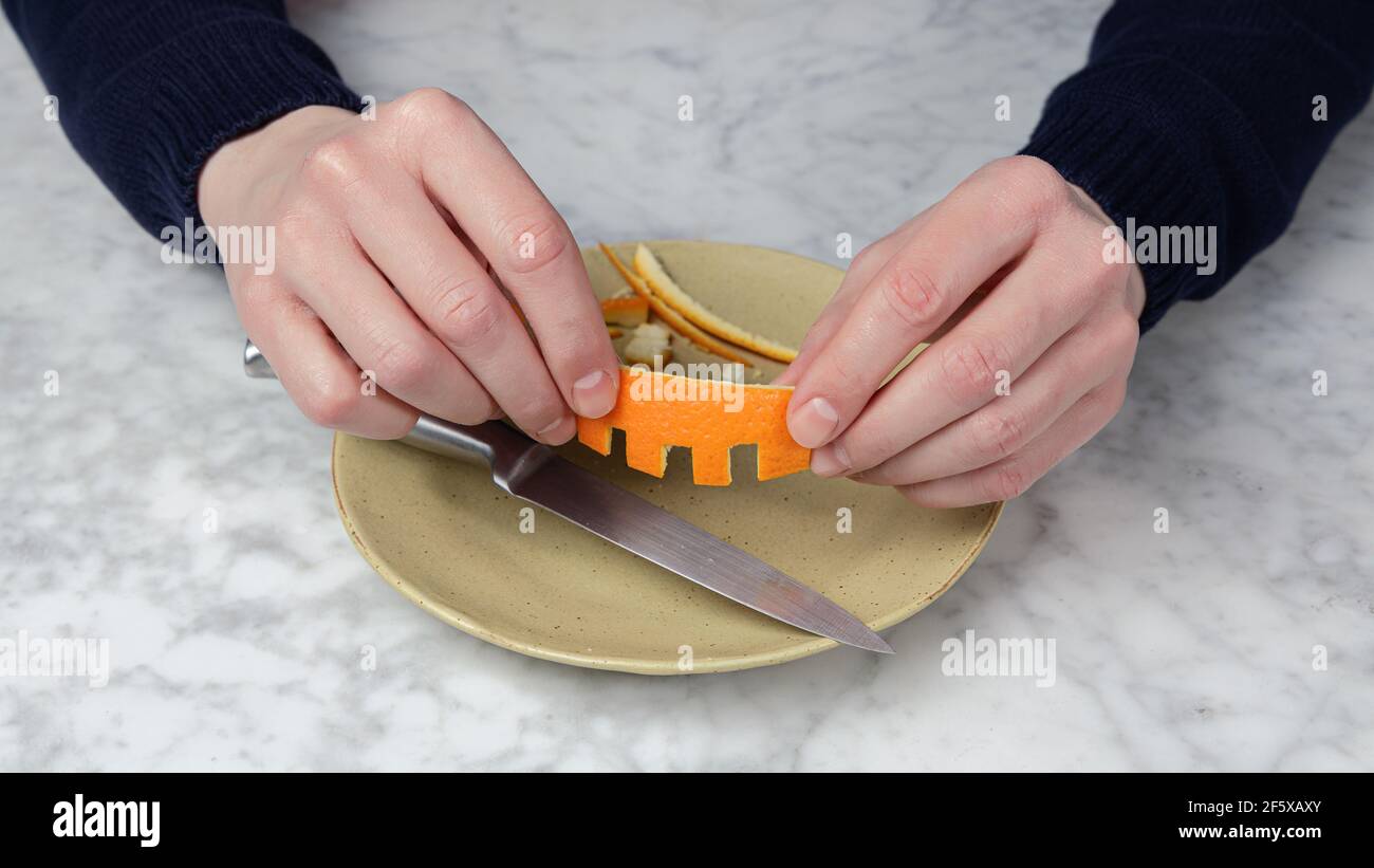 Man's hand cutting the skin of an orange with a knife. Fake teeth Stock Photo