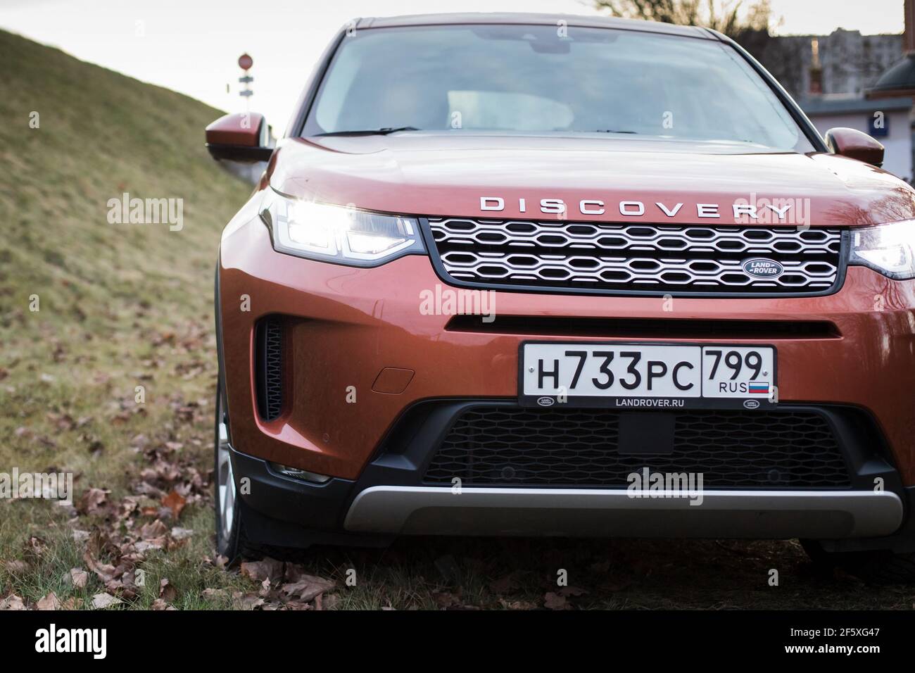 Moscow, Russia - December 20, 2019: Front side View of all new premium england suv. Land rover Discovery sport parked in the gray forest. Orange all wheel drive car standed on the ground. Stock Photo