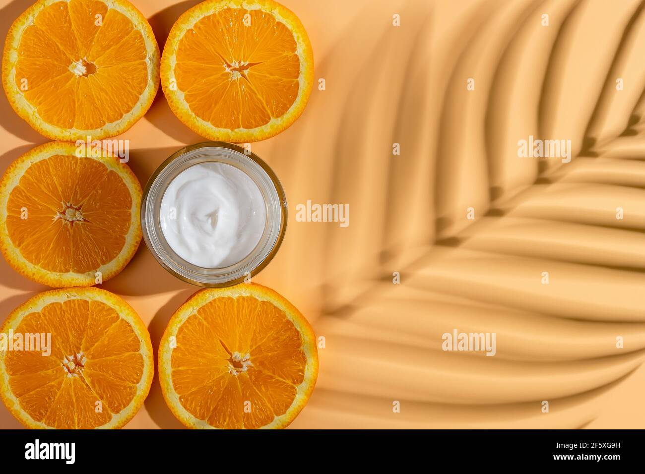Anti-wrinkle moisturizing face cream and juicy orange slices near blank surface with palm leaf shadow.Glass container of hydrating face cream. Stock Photo