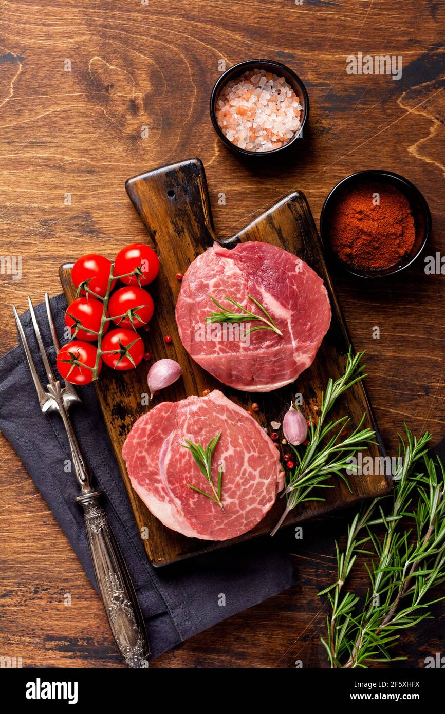 Two fresh Parisienne raw steak on wooden Board with salt, pepper and rosmary in a rustic style on old wooden background. Black angus. Top view Stock Photo