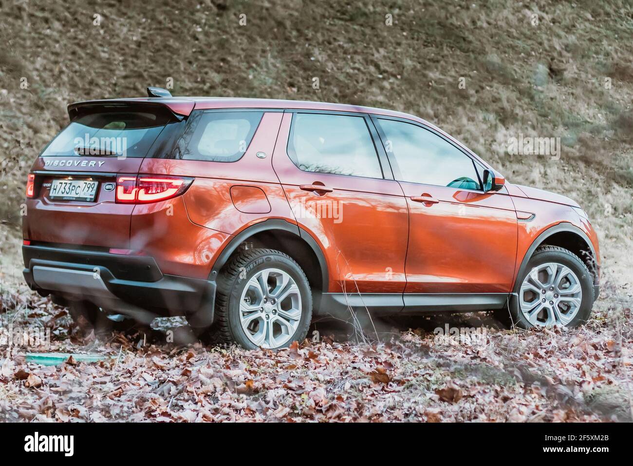 Moscow, Russia - December 20, 2019: Back side View of all new premium england suv. Land rover Discovery sport parked in the forest. Orange all wheel drive car standed on the ground. Stock Photo