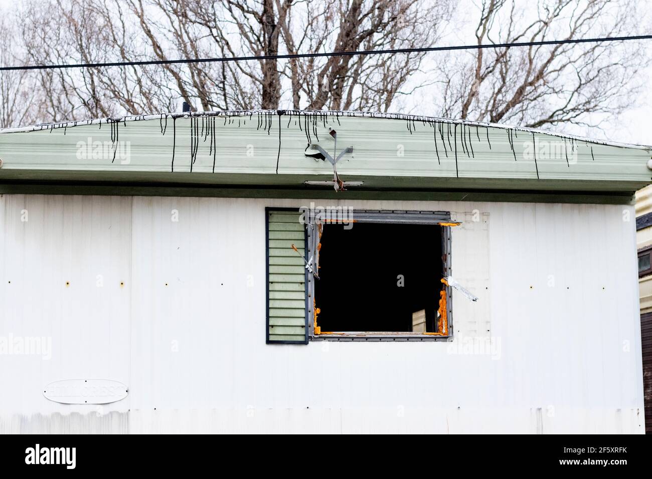 Horizontal picture of old abandoned green and white trailer with tar on roof and broken window Stock Photo